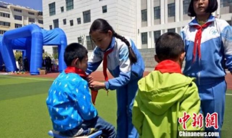 西寧市南川西路小學的少先隊員向兒童福利院的小朋友佩戴紅領巾。