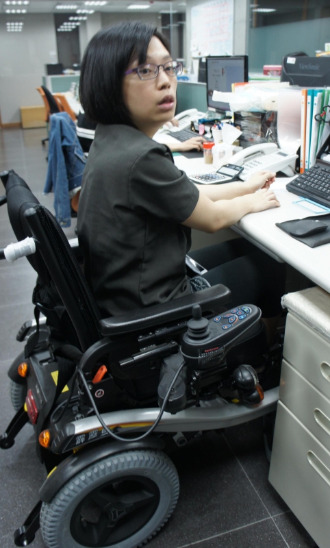 因小脑出血留有运动失调后遗症的小瑄，在劳工局协助提供电动轮椅排除职场障碍后，她乐在工作