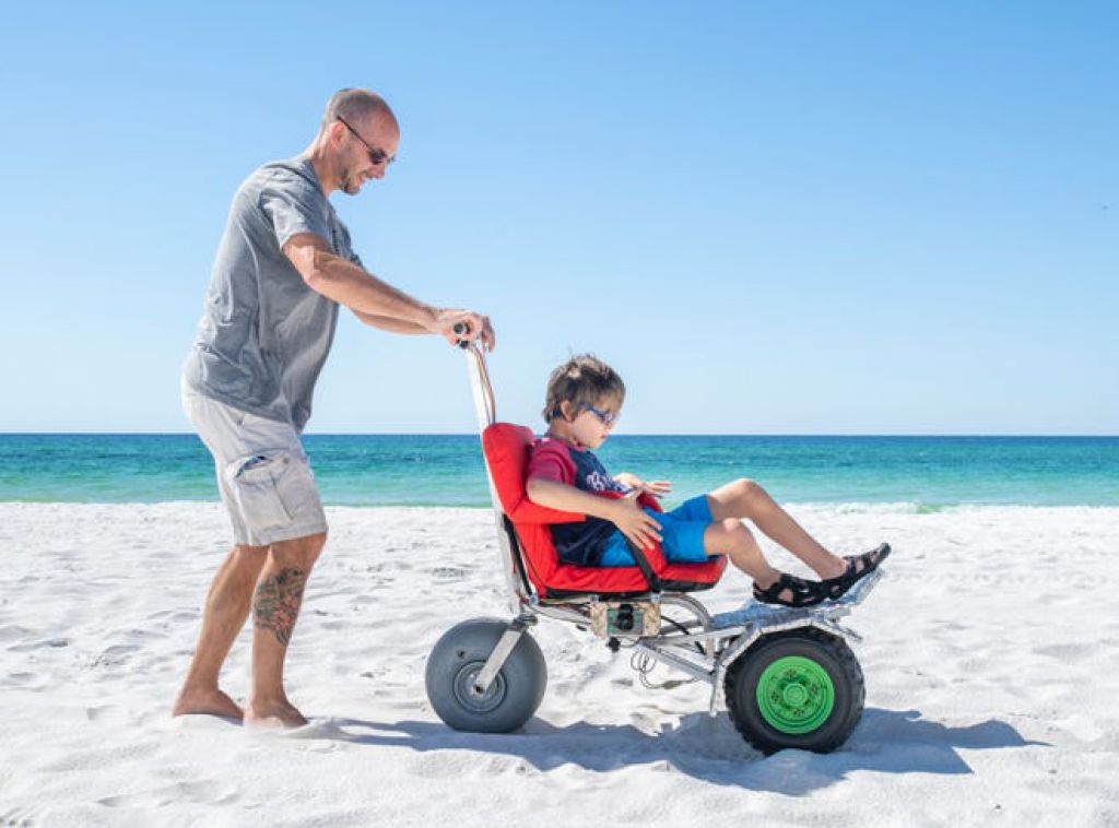特雷弗·丹顿（Trevor Denton）在纳瓦拉海滩（Navare Beach）上将他11岁的儿子克里斯蒂安·丹顿（Christian Denton）推上特制的电动沙滩轮椅。