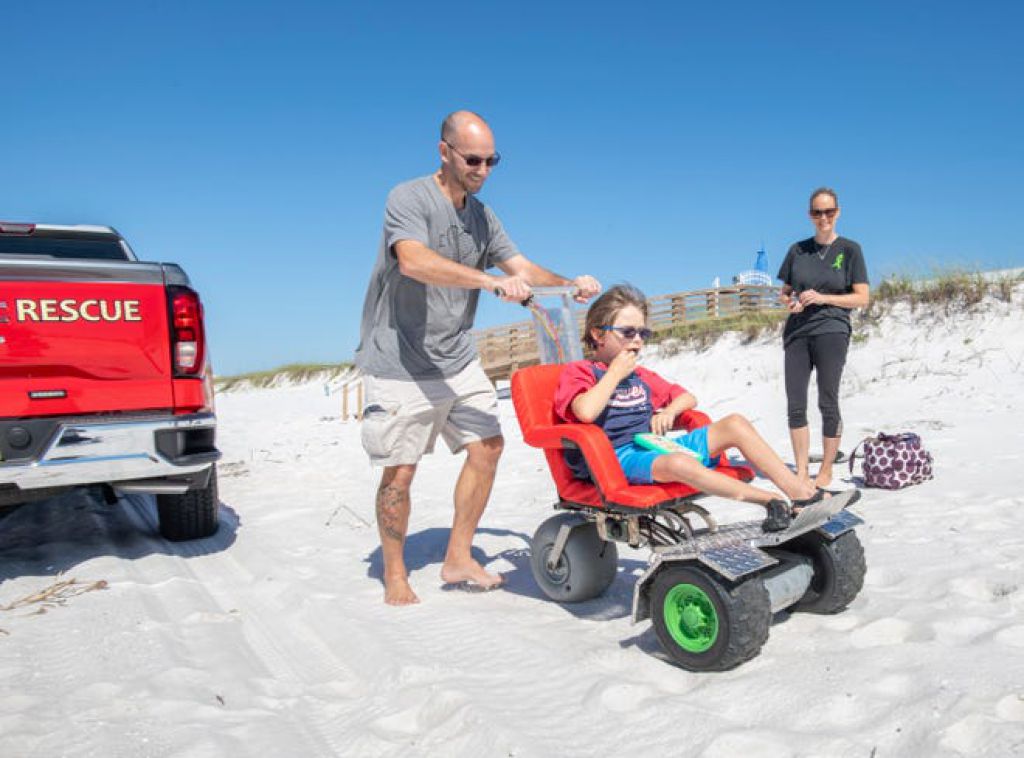朱莉·丹頓（Julie Denton）看著她的丈夫特雷弗·丹頓（Trevor Denton）在納瓦拉海灘的沙灘上沿著特製的電動輪椅推著他們11歲的兒子克里斯蒂安（Christian）。