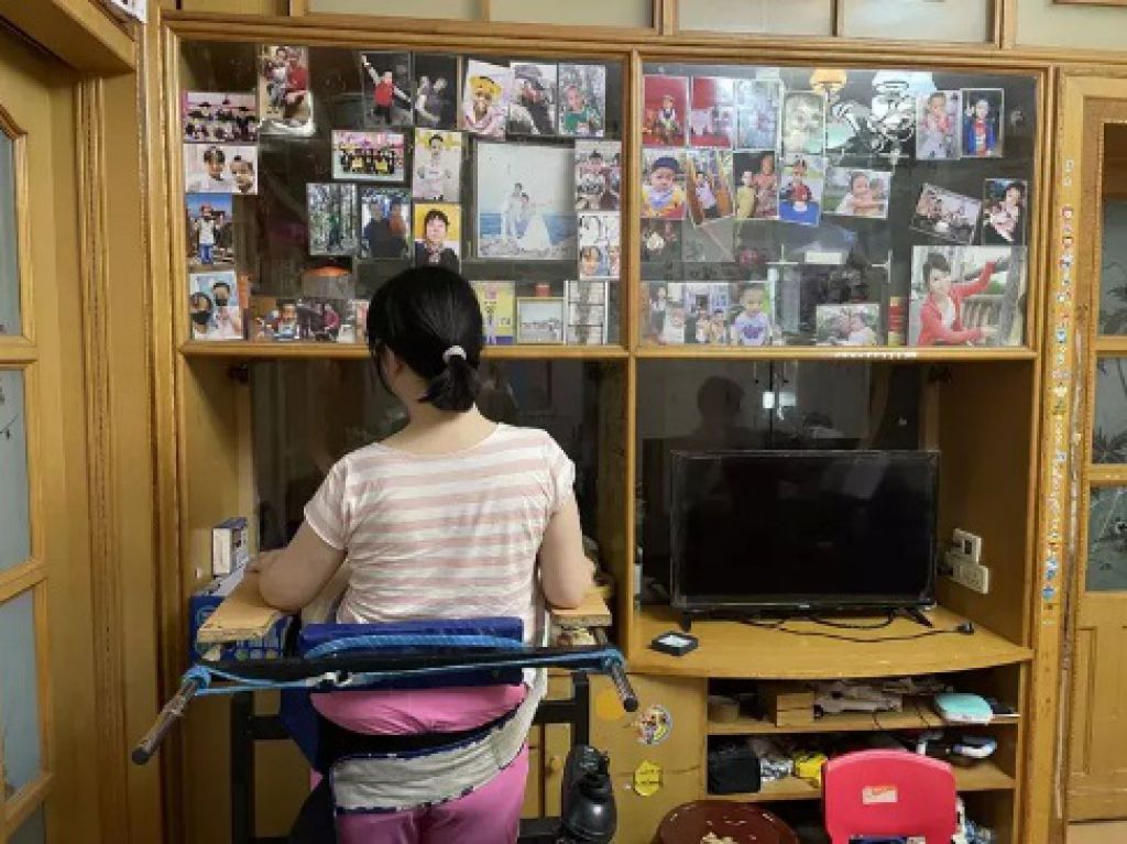 王磊在家裡進行站立訓練，對面的照片牆上貼著家人的照片。