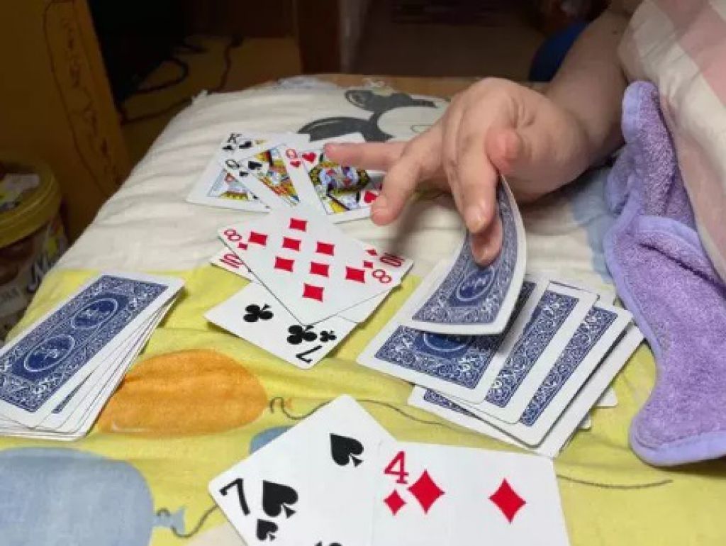 王磊在家裡，用僅剩的能拿物右手與孩子打牌。