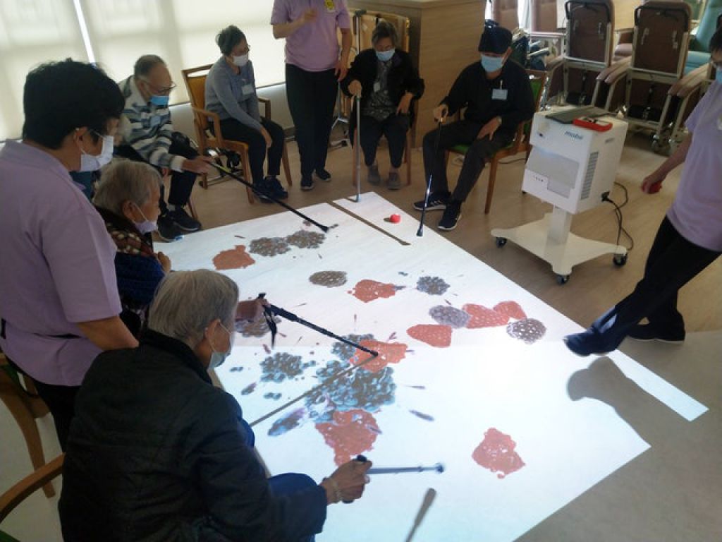 中心職業治療師與會員使用互動投影系統進行訓練，「品嚐」美味果汁。