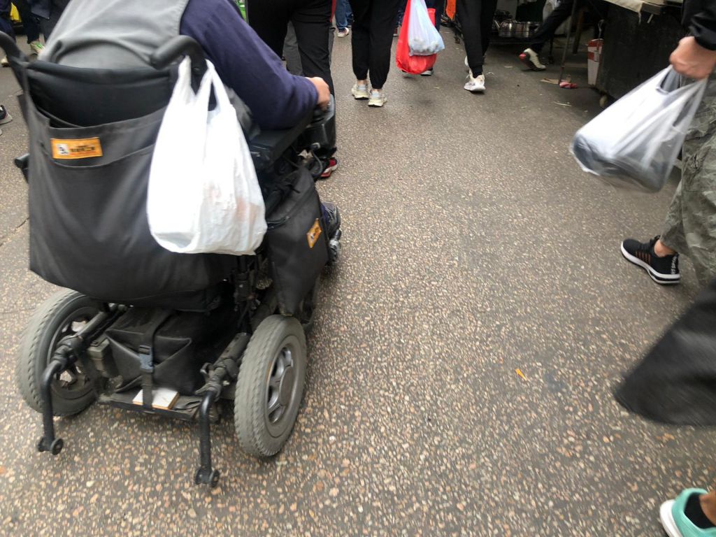Joyce坐着電動輪椅車，在街巿收巿時段趕緊買菜，以應付數日所需。